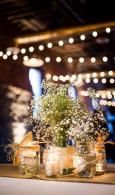 Glass jars with glowing candles and white flowers on a table beneath warm string lights at night