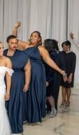 People in navy formal dresses pose in a bright indoor hall with draped curtains.