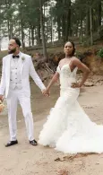 Bride and groom in white wedding outfits holding hands outdoors in a forest clearing