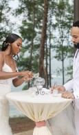 Couple signing a wedding document at a small outdoor table by the beach.