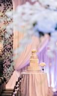 Tiered white wedding cake on a round table with pastel draped backdrop and floral decorations