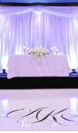 White draped wedding stage with floral centerpieces and projected monogram on the floor