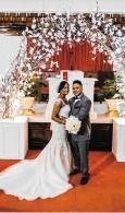 Bride and groom posing under a floral arch at a wedding reception, with red carpet decor