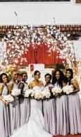 Row of women in silver gowns holding white bouquets before red and white floral backdrop