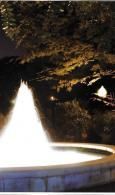Lit fountain spraying water at night in a tree-lined park