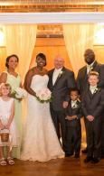Wedding group portrait in a warmly lit hall, with bride, groom, and family posing together