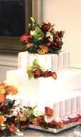 Three-tier white wedding cake decorated with colorful flowers and greenery