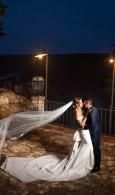 Couple kissing in wedding attire at night, with the bride’s veil flowing in the wind