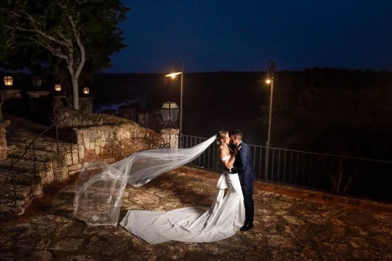 Bride and groom kissing outdoors at night, veil flowing in the wind.