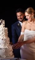 Bride and groom cut a tall white wedding cake in a dimly lit reception setting