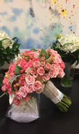 Pink rose bouquets in white paper on a dark table, with white flowers and a pastel floral backdrop
