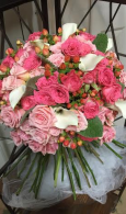Bouquet of pink and white roses with greenery in a clear vase, wrapped in white tulle