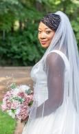 Bride in a white veil holding a pink bouquet outdoors, smiling over her shoulder
