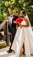 Bride and groom walking outdoors, bride holding a red bouquet and groom in a black tuxedo