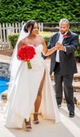 Bride in white gown holding red bouquet beside suited man at outdoor wedding ceremony