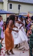 Two women dancing at an outdoor celebration, one in an orange dress and one in a white dress