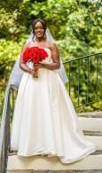 Woman in a white gown holding a red bouquet outdoors on a garden path