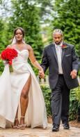 Wedding couple walking outdoors; bride in white gown holding red bouquet, groom in black suit.