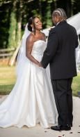 Bride and groom holding hands outdoors, smiling in a white wedding dress and black tuxedo.
