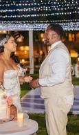 Couple in white outfits standing together at an outdoor evening reception under string lights