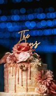 Decorated cake with pink flowers and gold topper against blurred blue lights