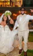Bride and groom in white wedding attire smiling and raising their arms outdoors at night