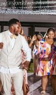 Couple in white and colorful outfits dancing at an indoor celebration under string lights
