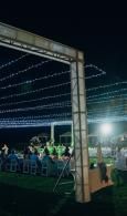 Nighttime outdoor event under string lights with people seated beneath a tented structure