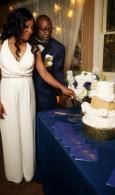 Couple cutting a white-and-blue tiered wedding cake beside a decorated table
