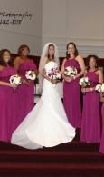 Bride in white gown standing with bridesmaids in magenta dresses holding bouquets on church steps