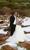 Bride and groom posing in wedding attire on snowy rocks beside a stream