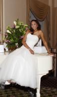 Woman in a white gown posing beside a white piano in an elegant room