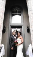Bride and groom posing at a church entrance, holding a bouquet, framed by tall dark doorways