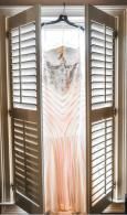 Wedding dress hanging in an open closet with white shutters