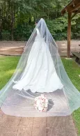 Bride in a long white veil and gown walking on a path outdoors, holding a bouquet.