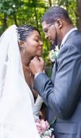 Bride and groom gently holding hands and touching foreheads in a soft outdoor wedding portrait