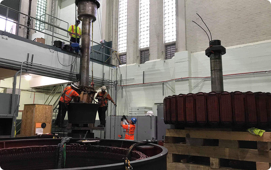 Workers disassemble a large generator in a tall industrial building.