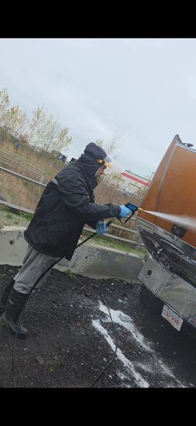 Yellow construction loader tire being sprayed clean with water, muddy ground visible.