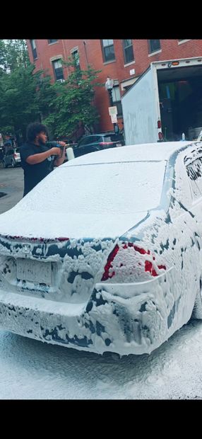 Person washing a black car with a pressure washer outdoors