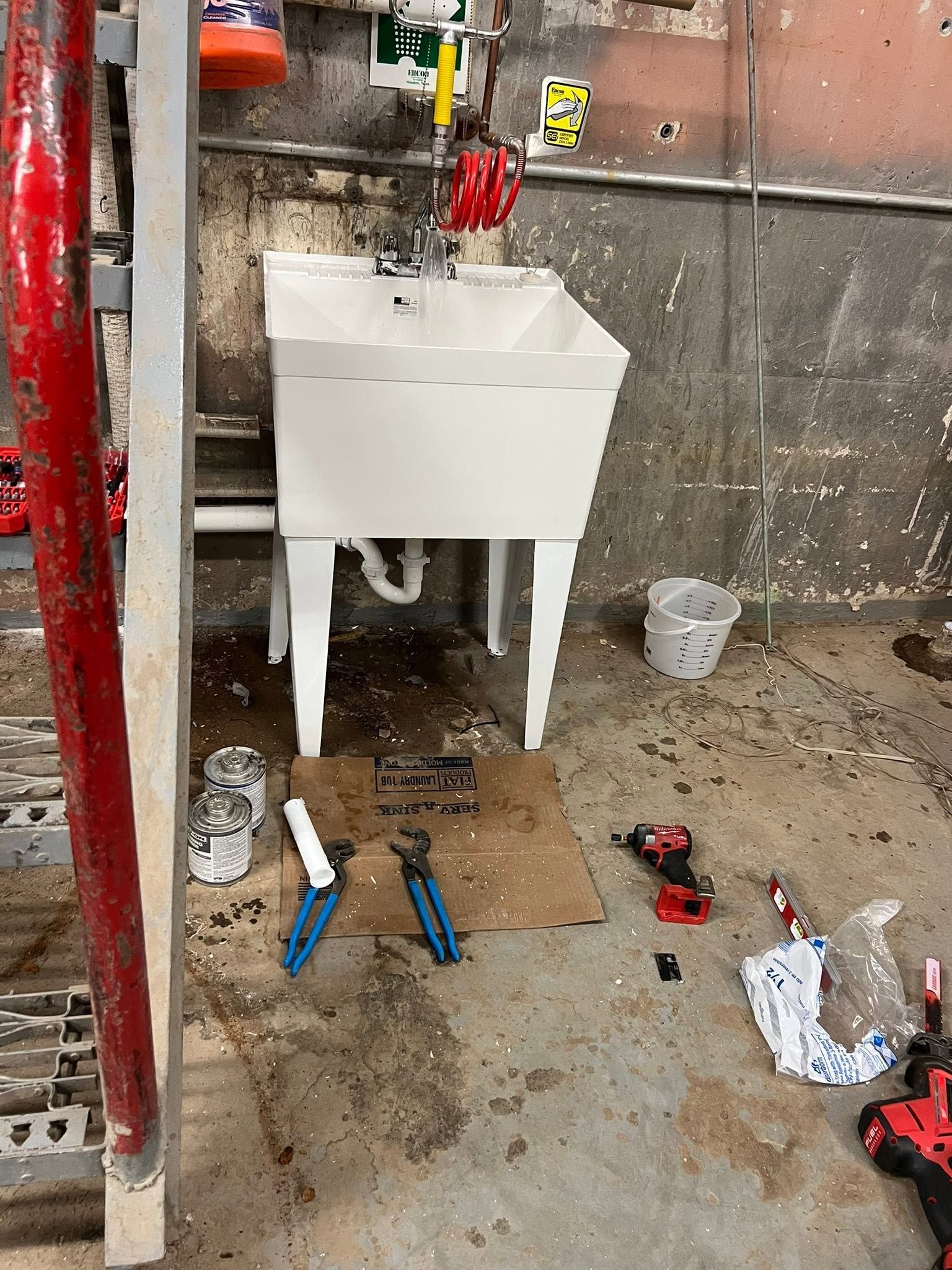 White utility sink on a construction floor with tools and debris around it.