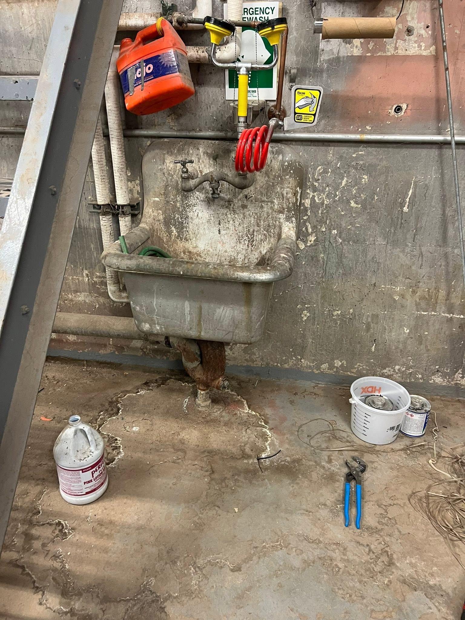 Construction work area with a utility sink, tools, paint cans, and concrete floor debris