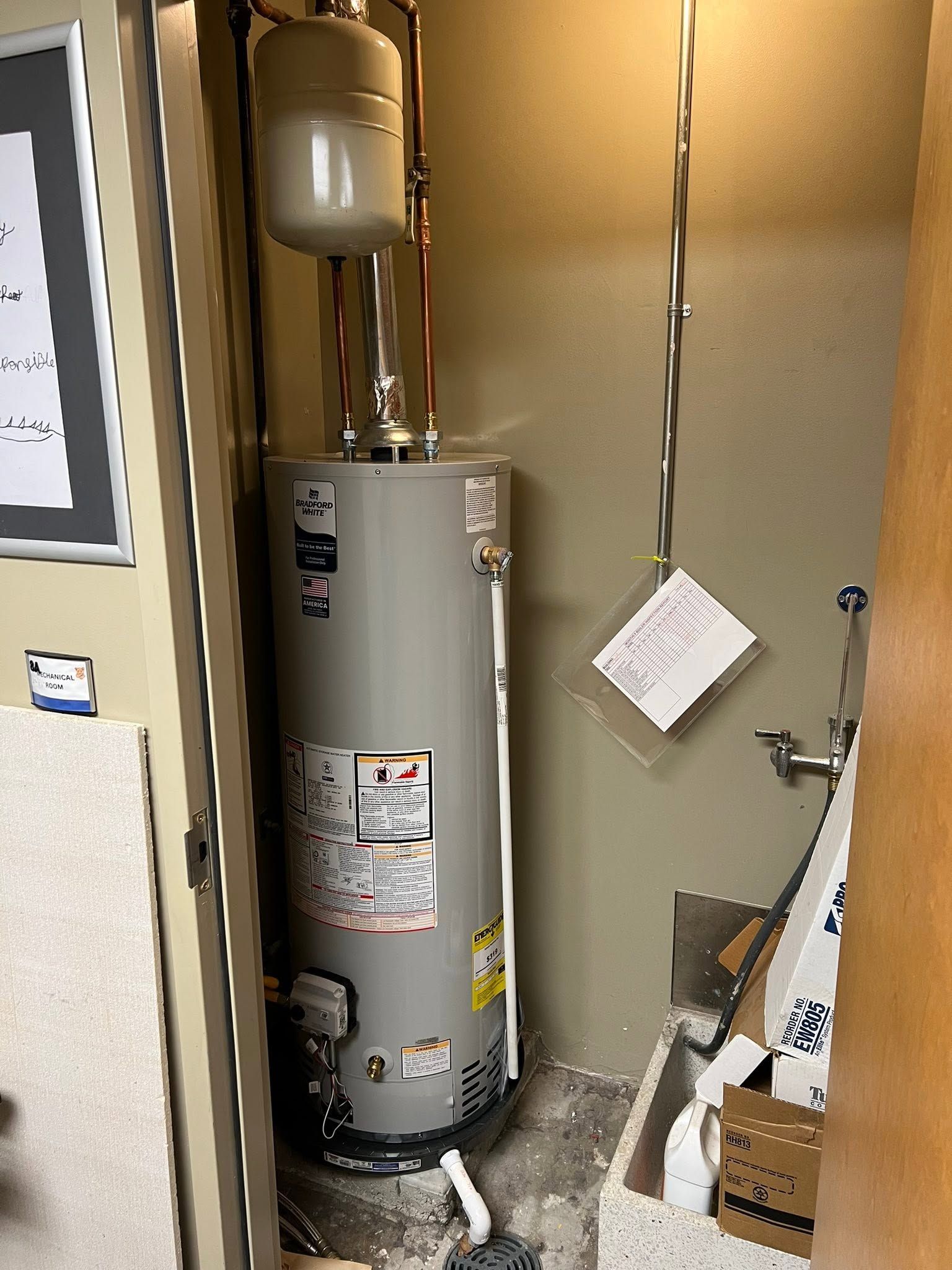 Water heater in a small utility closet with hanging cords and scattered boxes.