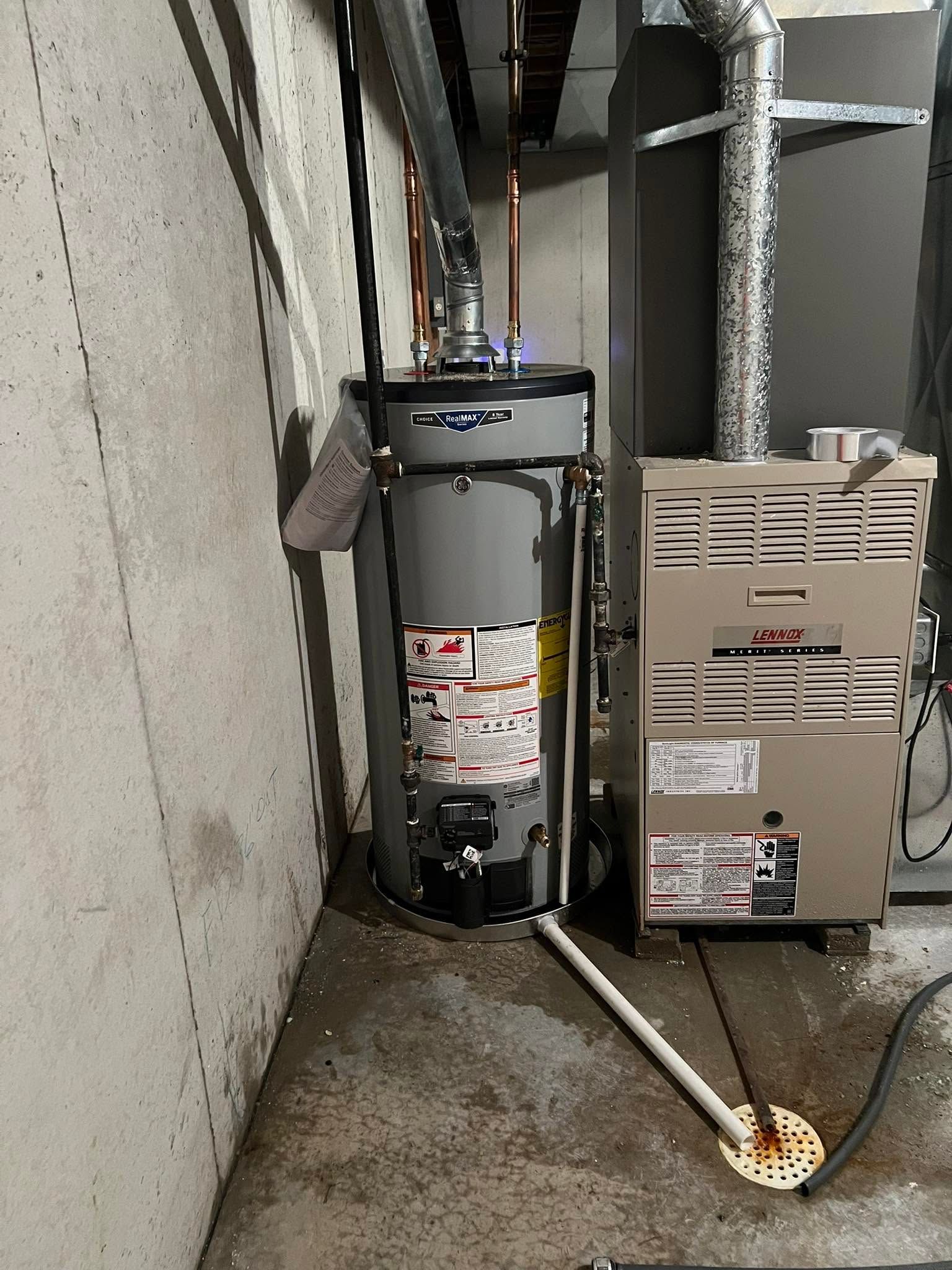 Water heater and furnace in a narrow utility area with a metal pipe on the floor and a floor drain cover.