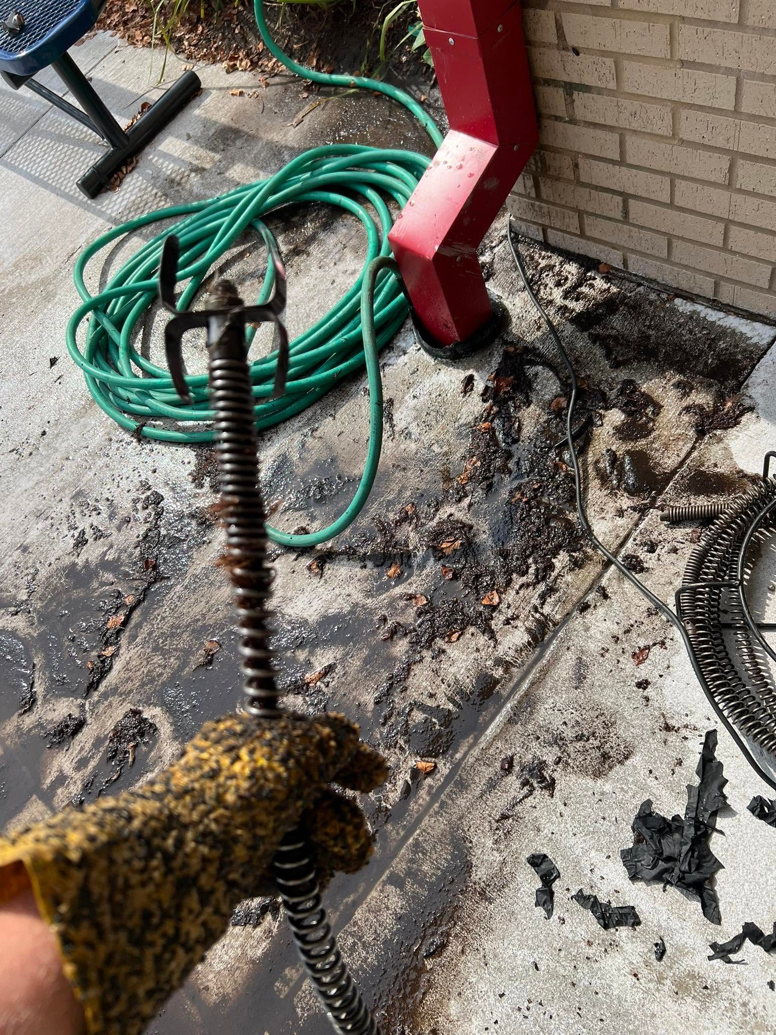 Soaked concrete floor with mud, a green hose, and a gloved hand holding a coiled cable tool