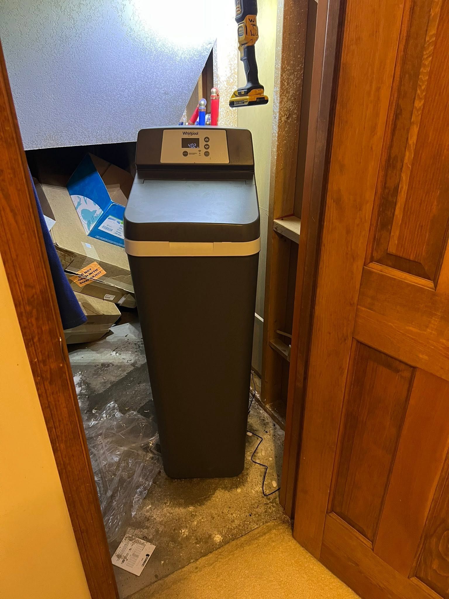 A tall black trash bin in a narrow doorway with cardboard and clutter around it.