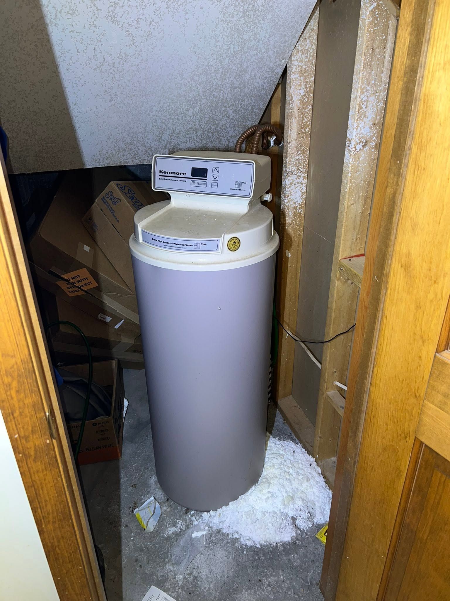 Water heater in a cramped attic space with insulation and snow-like debris on the floor.