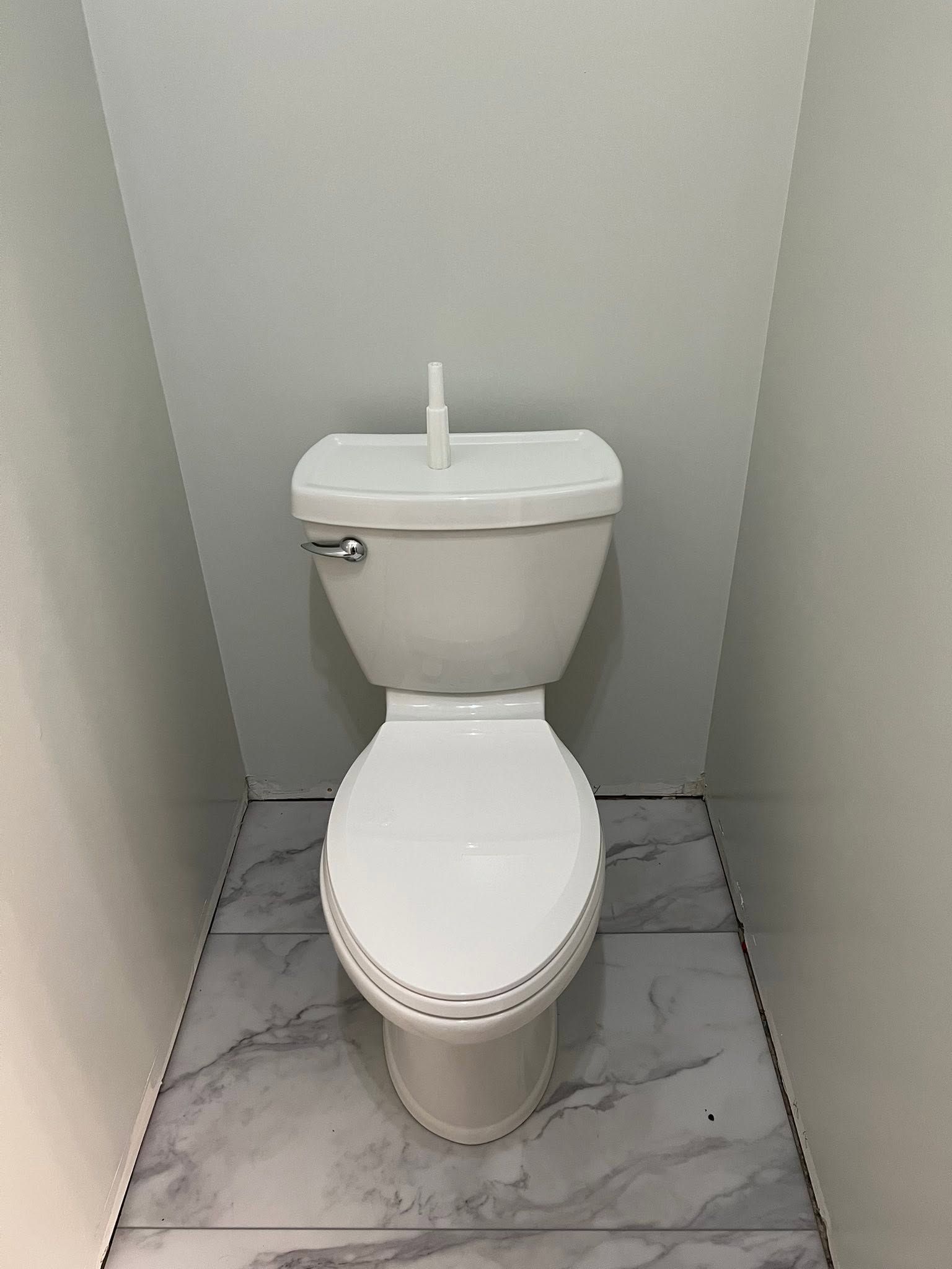 Small white toilet in a narrow gray-tiled bathroom stall.