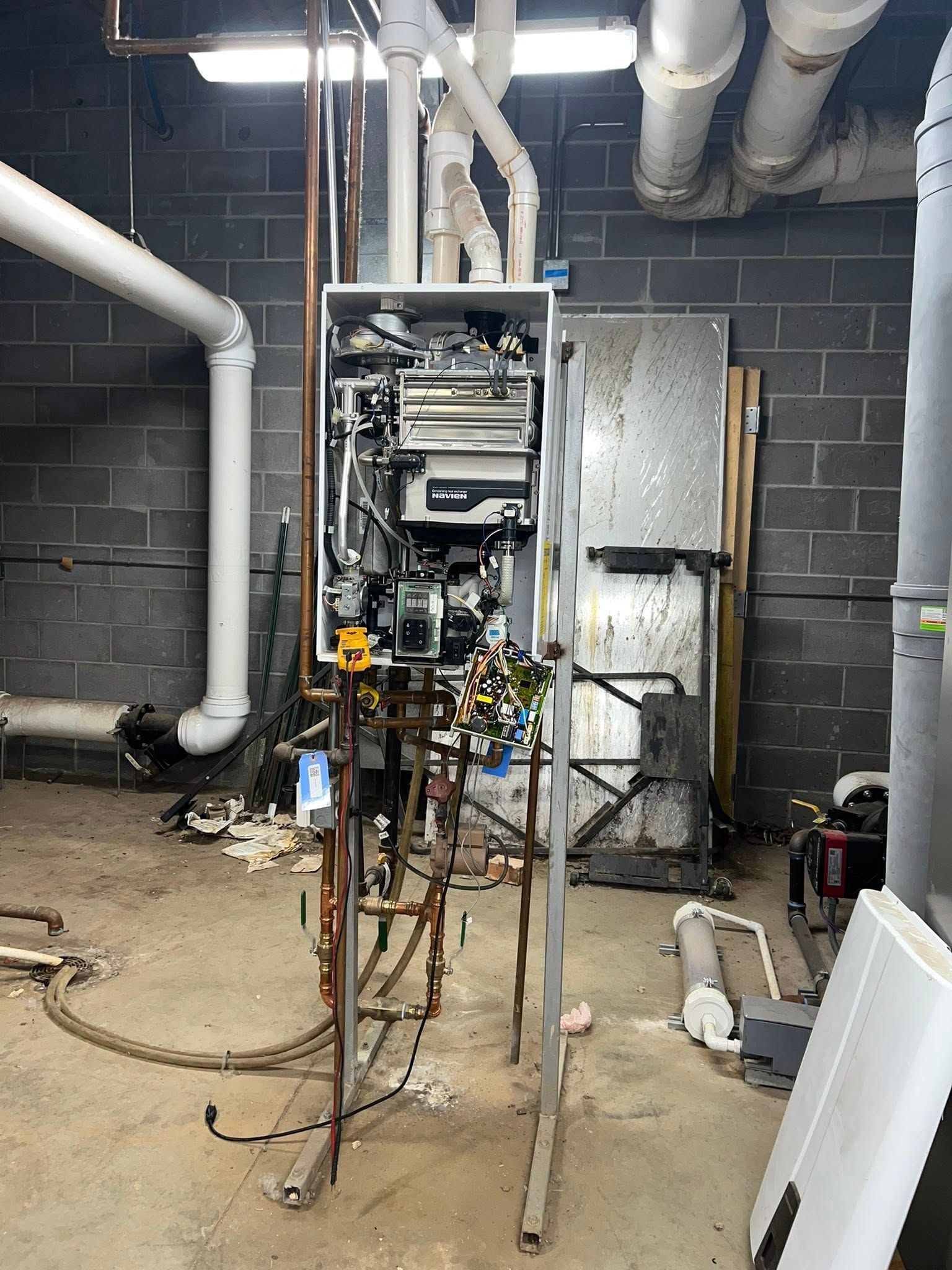 Mechanical equipment in a basement utility room with exposed pipes and a metal cabinet on the wall