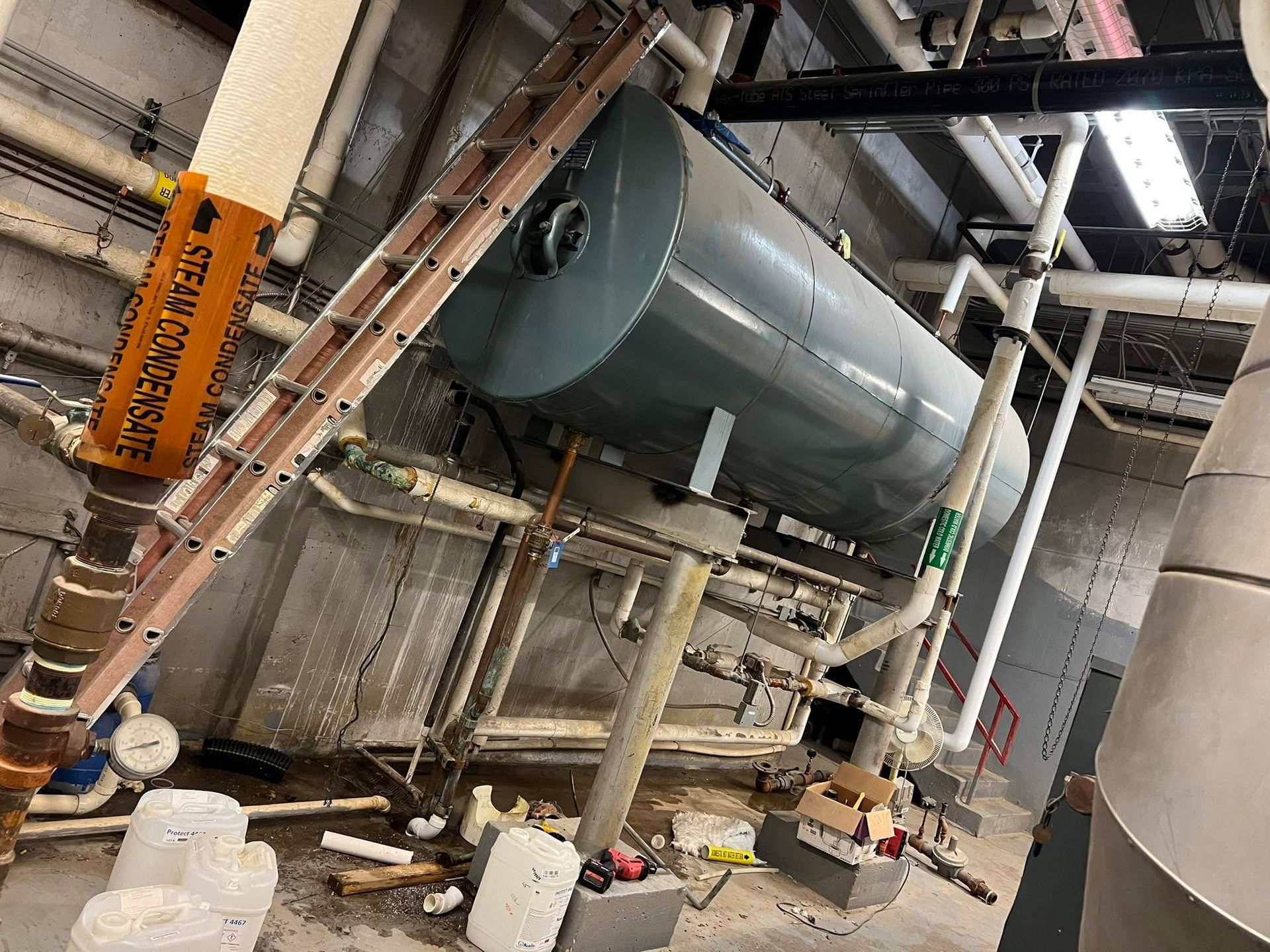 Industrial machinery and piping in a factory, with a large green tank on a metal frame