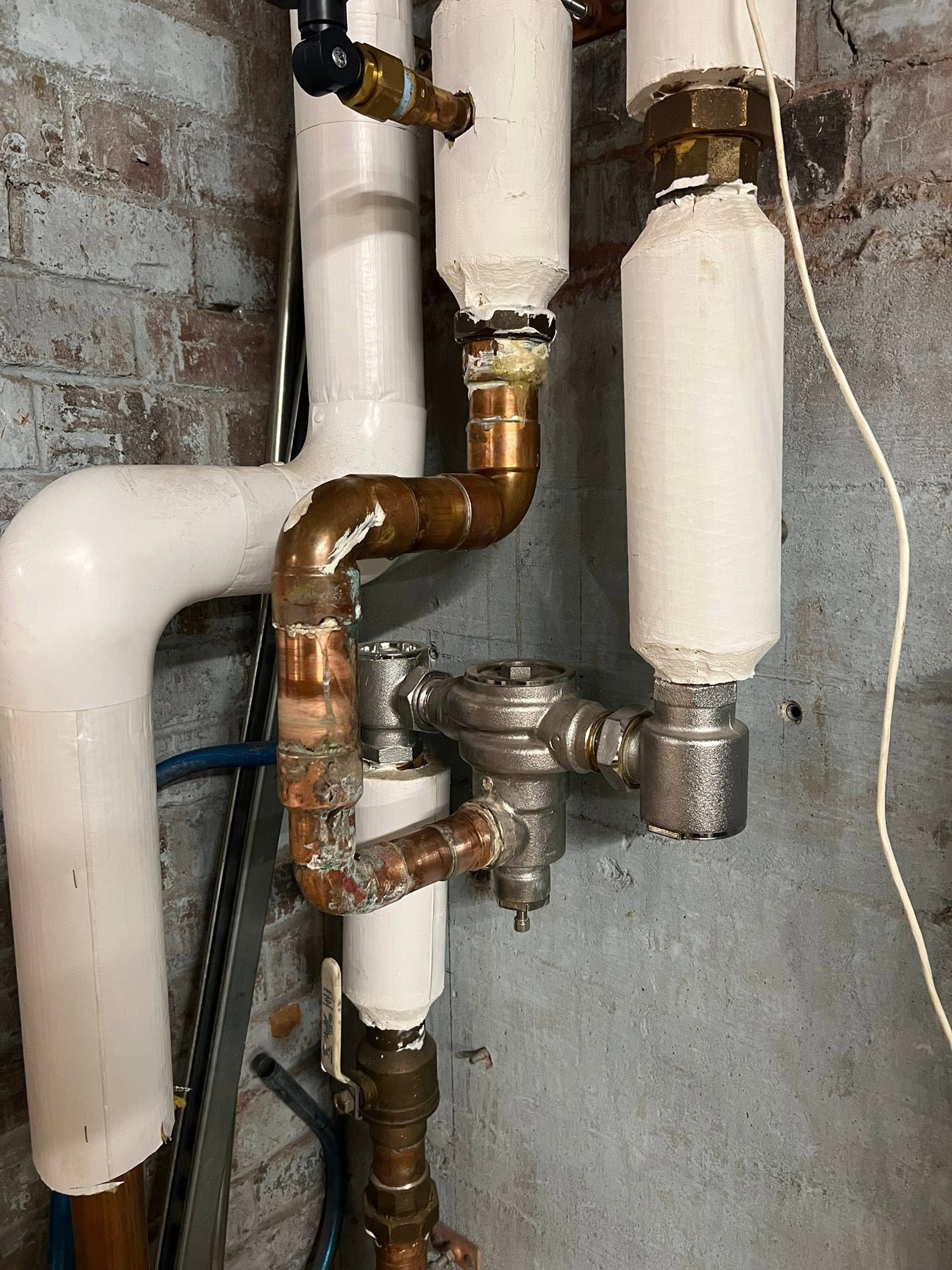 Rusty plumbing pipes and valves connected to a wall with white insulation and a drain line